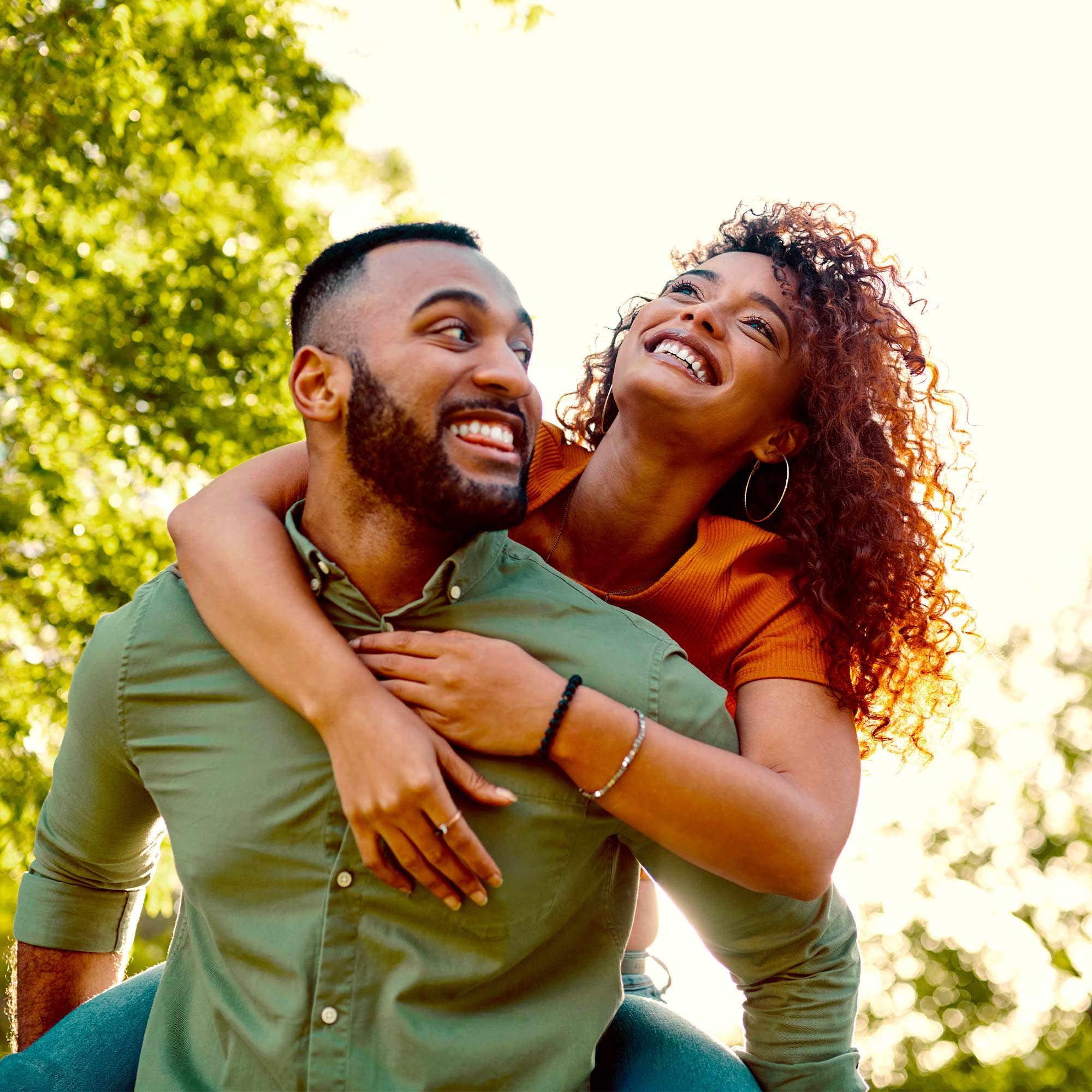 A man gives a piggyback ride to a woman and they both smile.